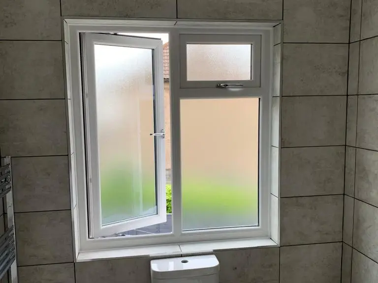 A white casement window with frosted glass fitted in a tiled bathroom