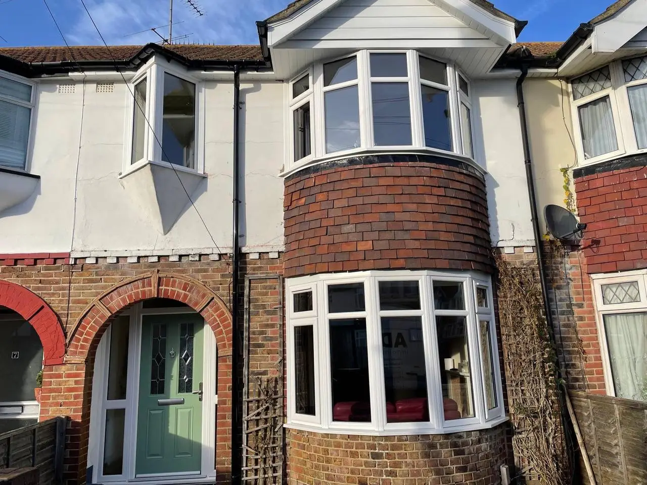 A bay-fronted terraced house with new white bay windows, white boards along the roof edge and a sage green front door