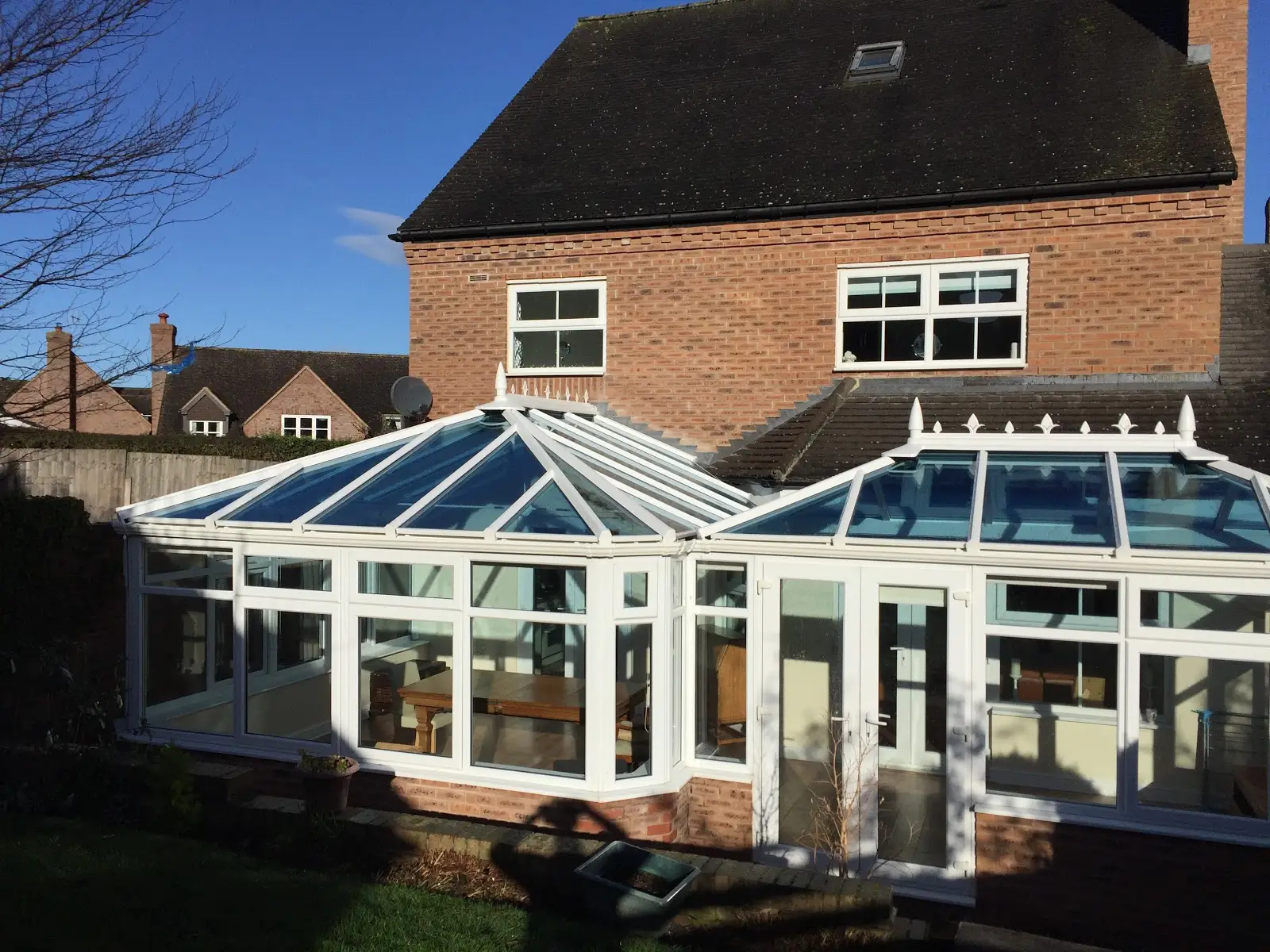 A large white conservatory with two glass roofs across the back of a brick house