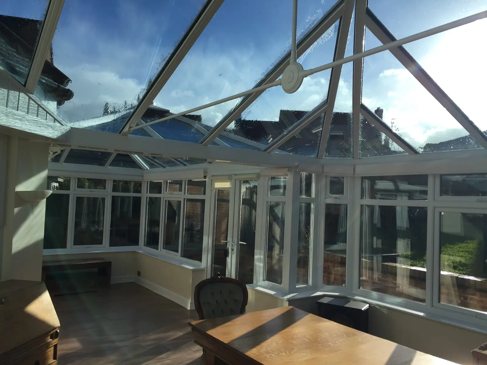 Inside a white conservatory with a glass lantern roof, dining table and doors open to the garden