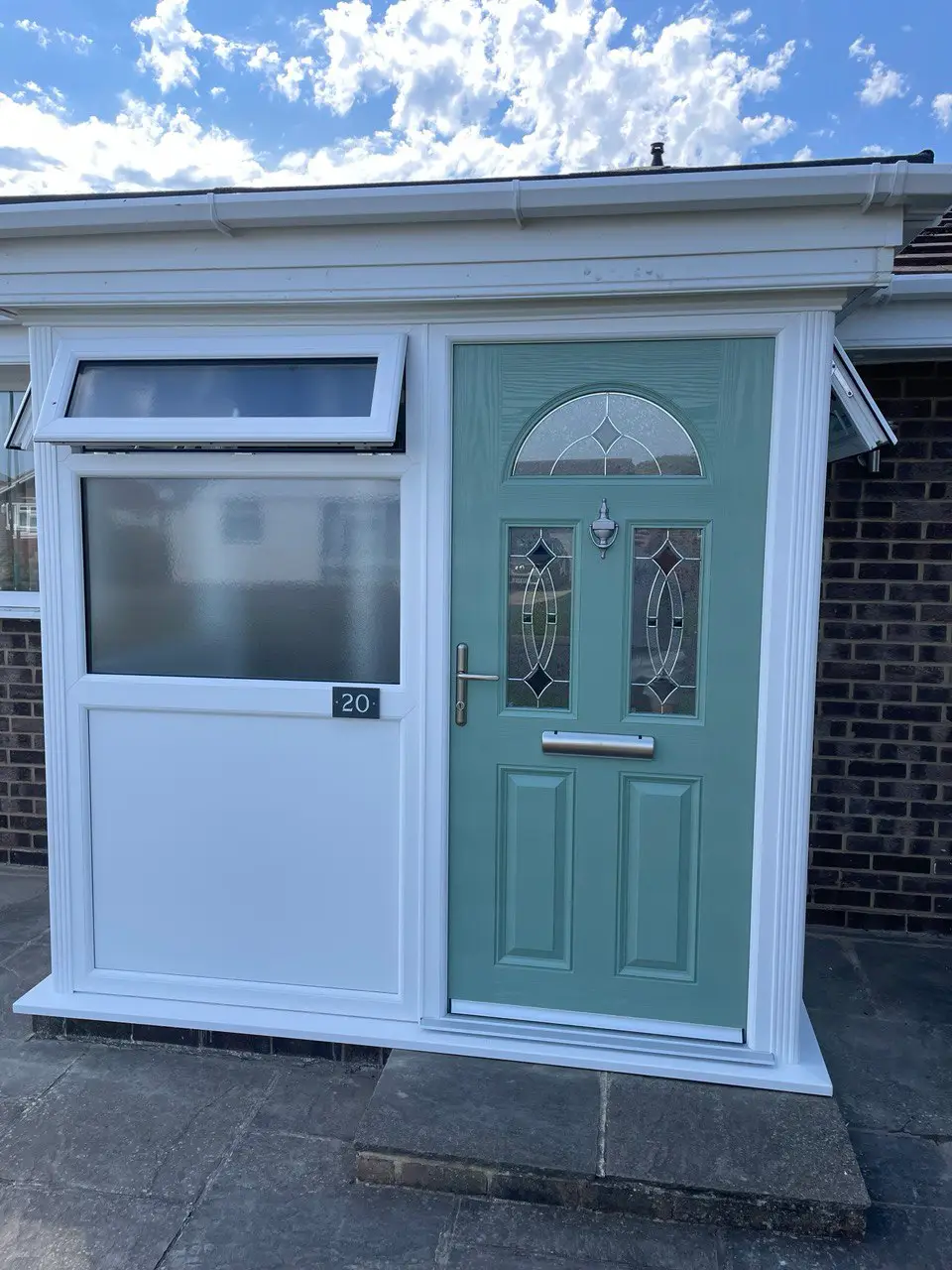 A white porch with a sage green composite front door and a frosted glass side panel