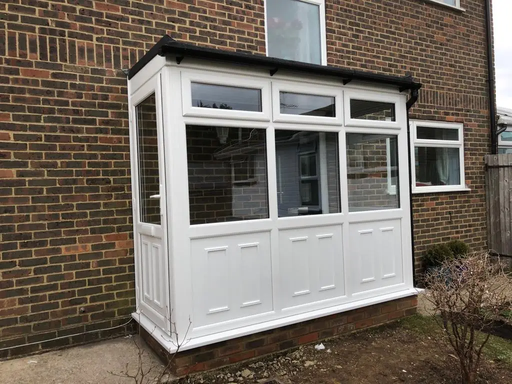 A white porch with raised panels and clear glass, built onto a brick house