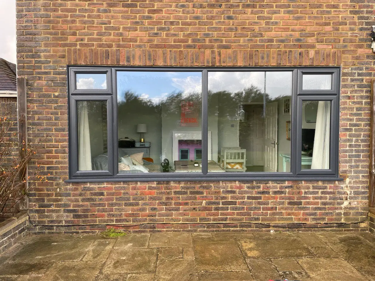 A wide anthracite grey window with slim frames set into a brick wall